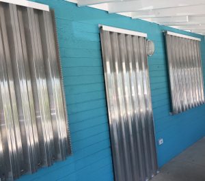 A small turquoise cottage in Florida has hurricane shutters on the front windows and door to secure the home during a Hurricane warning.